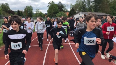 Kinder mit Nummerierung laufen auf einem Sportplatz