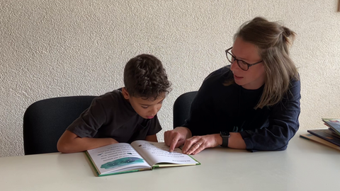 Junge sitzt mit Lesepatin an einem Tisch