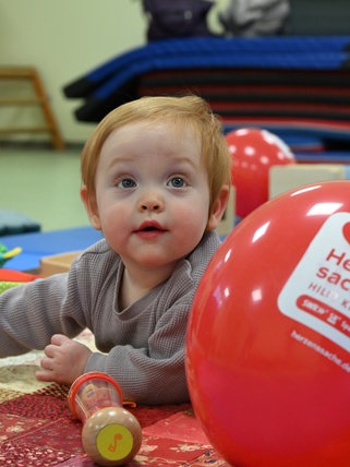 Clara liegt auf einer Spielmatte, vor ihr ein roter Herzenssache-Luftballon