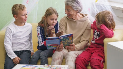 Lesepatin sitzt mit drei Kindern auf einem Sofa