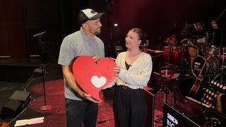Max Mutzke und Vivi schauen einander an und halten ein rotes Herz in den Händen
